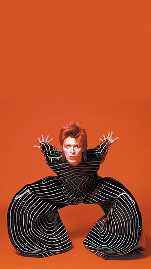 David Bowie in a dramatic black and white striped outfit against a bold orange background HD phone wallpaper