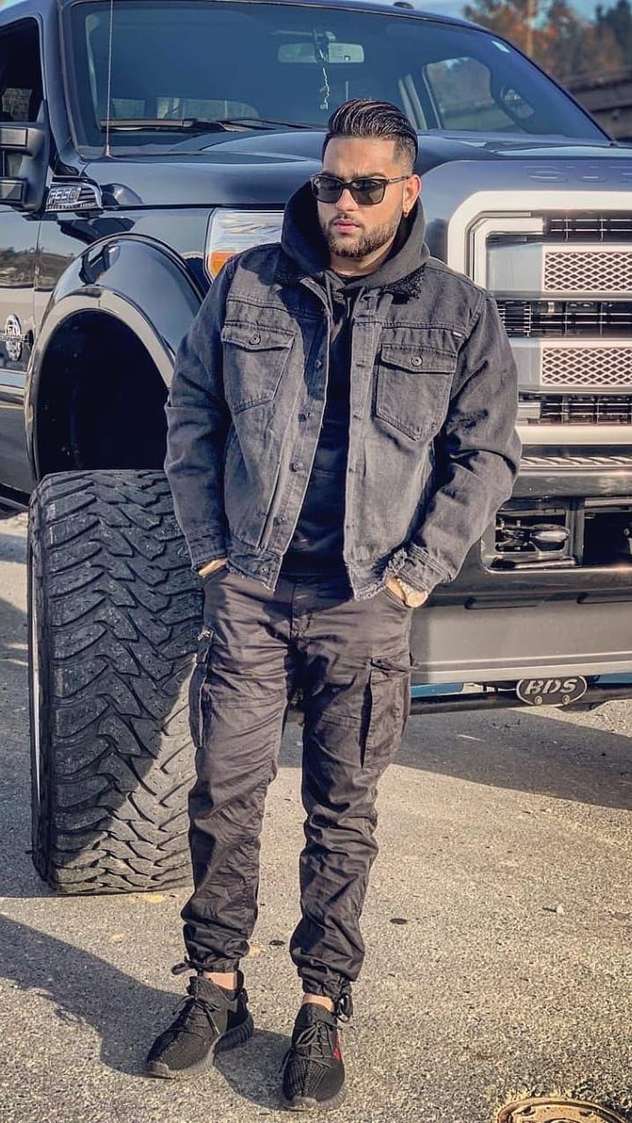 Karan Aujla in Black Denim Jacket and Cargo Pants Standing Before a Lifted Ford F-150 HD phone wallpaper