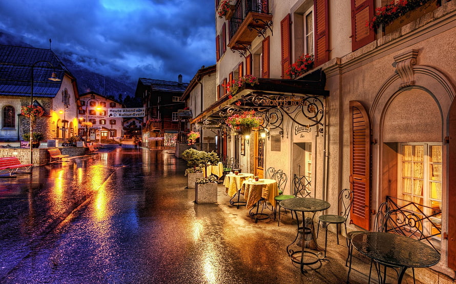 Rainy Evening Street Scene in a Swiss Alpine Town with Cafe and Warm Lights HD wallpaper