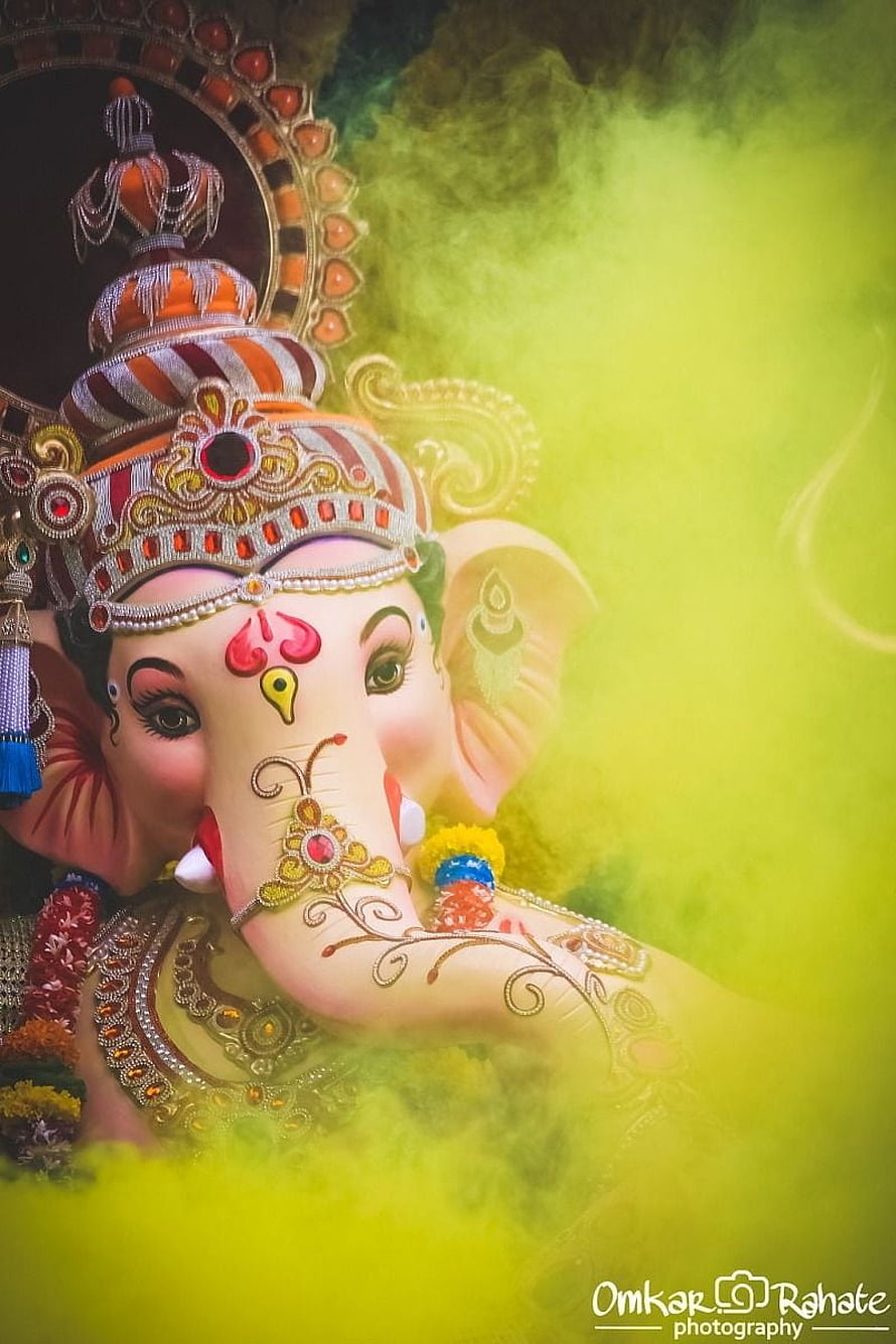 Lord Ganesha adorned in ornate jewelry and crown against a vibrant yellow smoke background HD phone wallpaper
