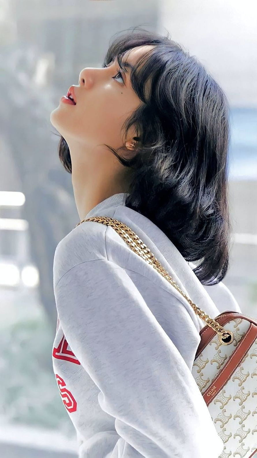 Lisa from BLACKPINK in a grey sweatshirt with a Celine chain bag, looking upward in soft natural light HD phone wallpaper