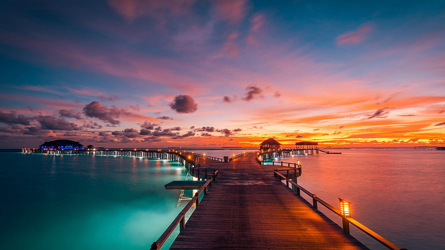 Maldives Overwater Resort Pier at Sunset with Vibrant Sky and Turquoise Lagoon HD wallpaper