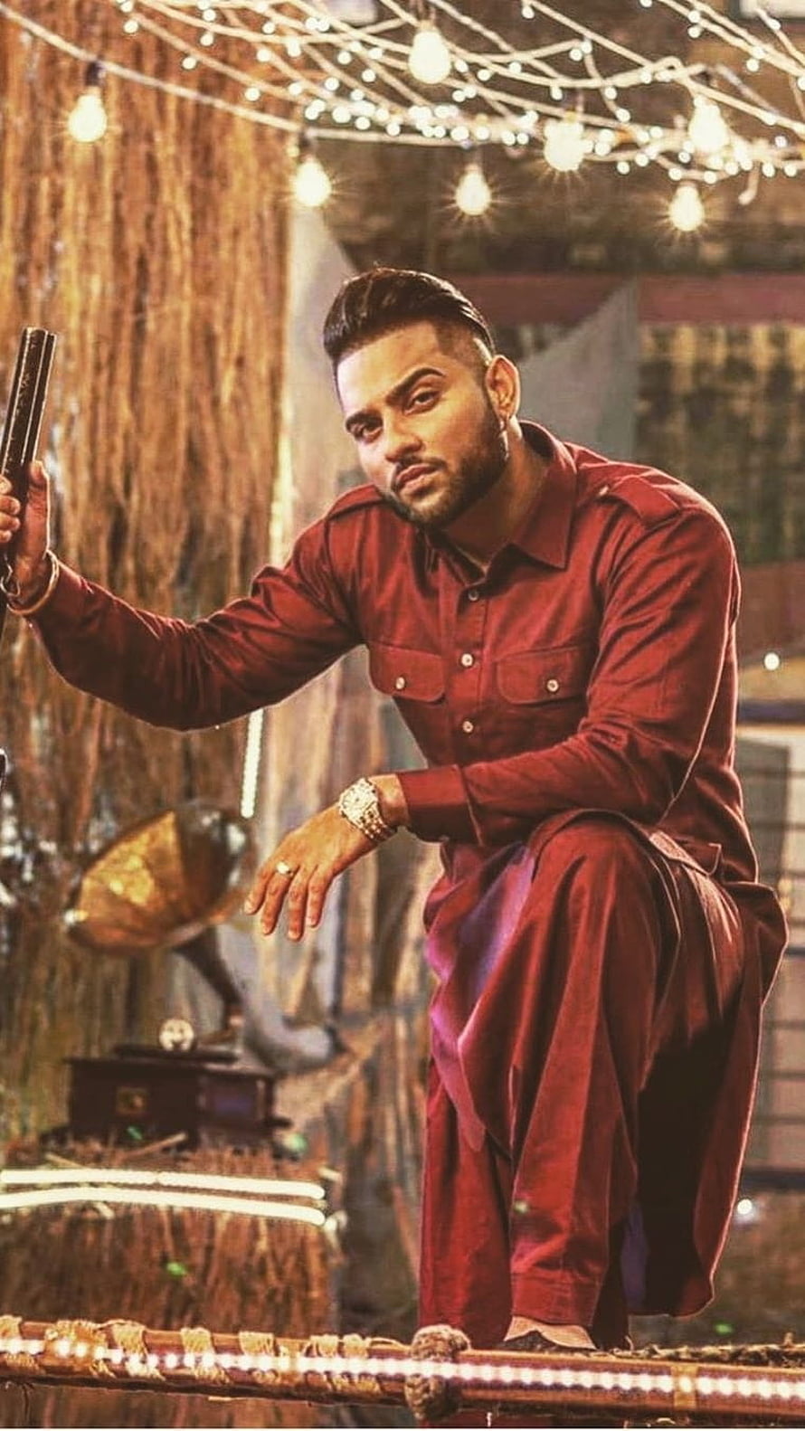 Karan Aujla in a red kurta holding a pistol under warm string lights HD phone wallpaper