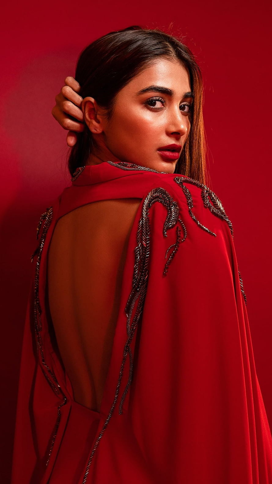 Pooja Hegde in a red embroidered cape with open back against a deep red studio backdrop HD phone wallpaper