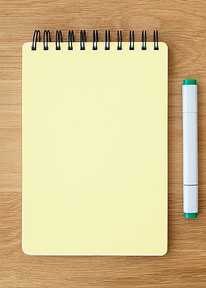 Blank yellow spiral notebook with white marker on wooden desk surface HD phone wallpaper