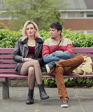 Young couple sitting on a purple park bench in casual streetwear with green foliage background HD phone wallpaper
