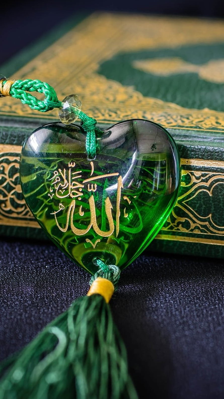 Green Heart-Shaped Amulet with Gold Arabic Calligraphy Resting on an Ornate Quran HD phone wallpaper
