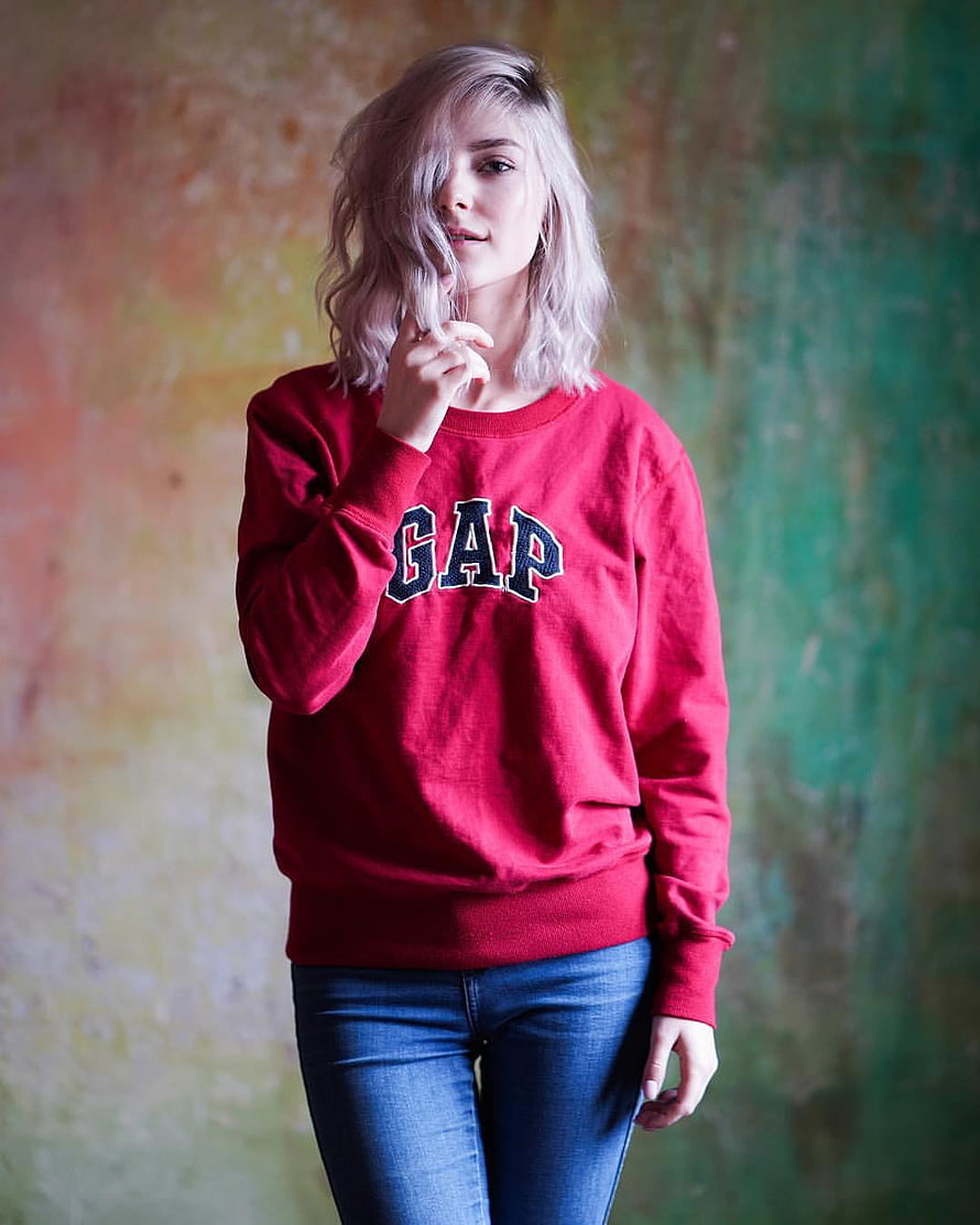 Eva Elfie in a Red Gap Sweatshirt and Blue Jeans Against a Textured Wall HD phone wallpaper