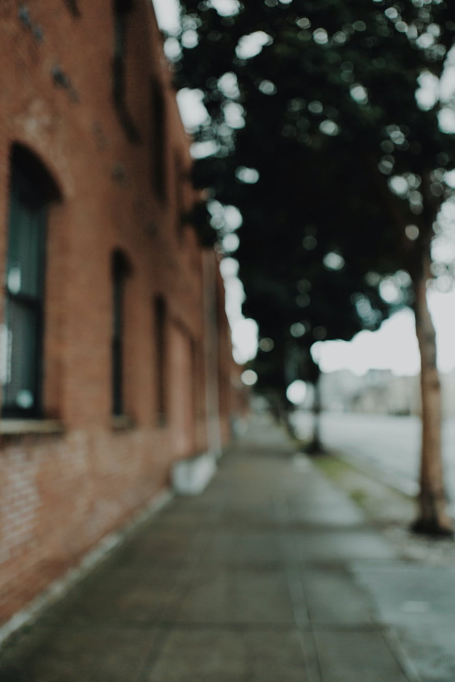 Soft Focus Urban Sidewalk Along a Red Brick Building with Blurred Trees HD phone wallpaper