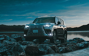 Lexus LX 600 SUV on Rocky Shoreline at Dusk with Headlights On HD wallpaper