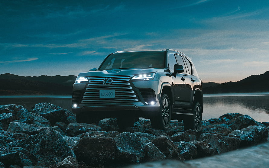 Lexus LX 600 SUV on Rocky Shoreline at Dusk with Headlights On HD wallpaper