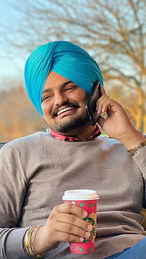 Sidhu Moose Wala smiling while talking on phone and holding a coffee cup outdoors HD phone wallpaper