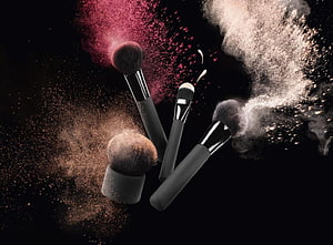 Dramatic makeup brushes with colorful powder bursts on a dark background HD wallpaper