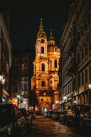 Illuminated Baroque Church Tower Rising Over Cobblestone Street at Night in European City HD phone wallpaper