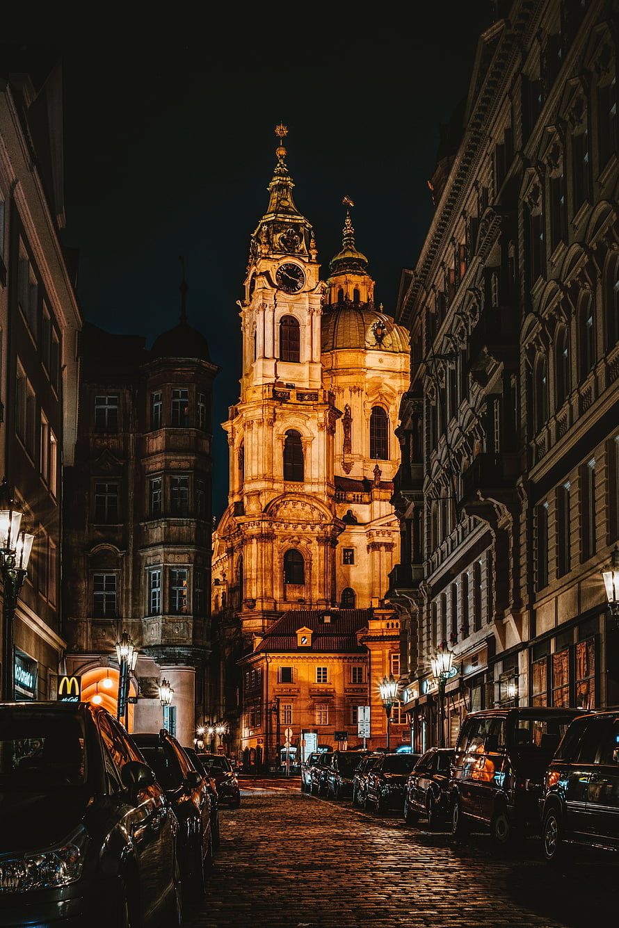Illuminated Baroque Church Tower Rising Over Cobblestone Street at Night in European City HD phone wallpaper
