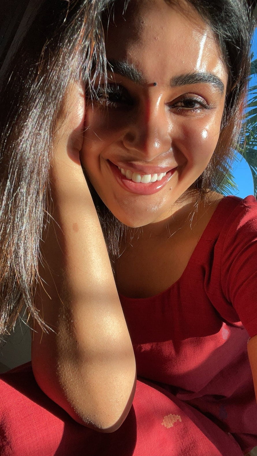 Samyukta Menon in a red top smiling outdoors with palm trees and bright sunlight HD phone wallpaper