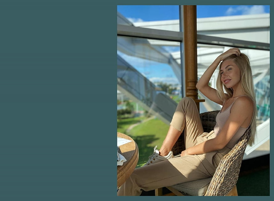 Blonde woman in beige outfit sitting in wicker chair by large window with garden view HD wallpaper