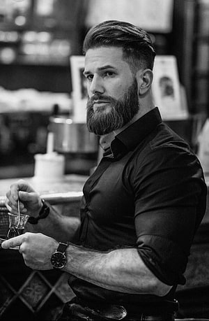 Bearded Man in Black Shirt Holding a Glass in a Bar Setting HD phone wallpaper