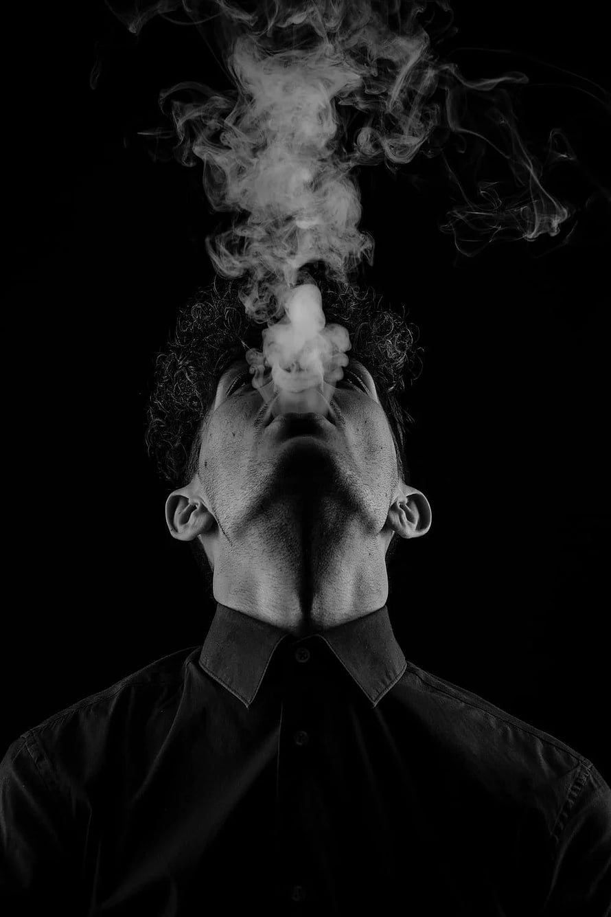 Black and White Portrait of a Man Releasing Smoke Against a Dark Background HD phone wallpaper