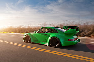 Widebody Green Porsche 911 Turbo with Large Rear Wing Driving on Open Highway at Sunset HD wallpaper
