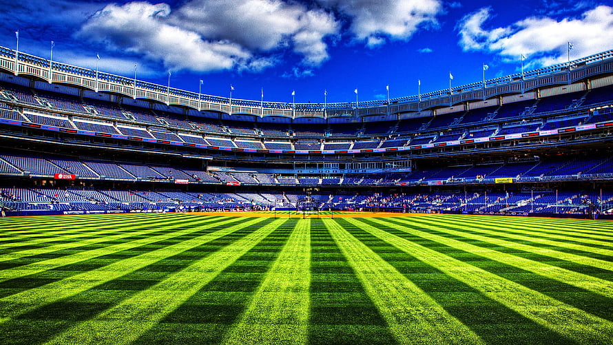 Vibrant Green Football Field Inside a Large Blue Seated Stadium Under a Bright Sky HD wallpaper