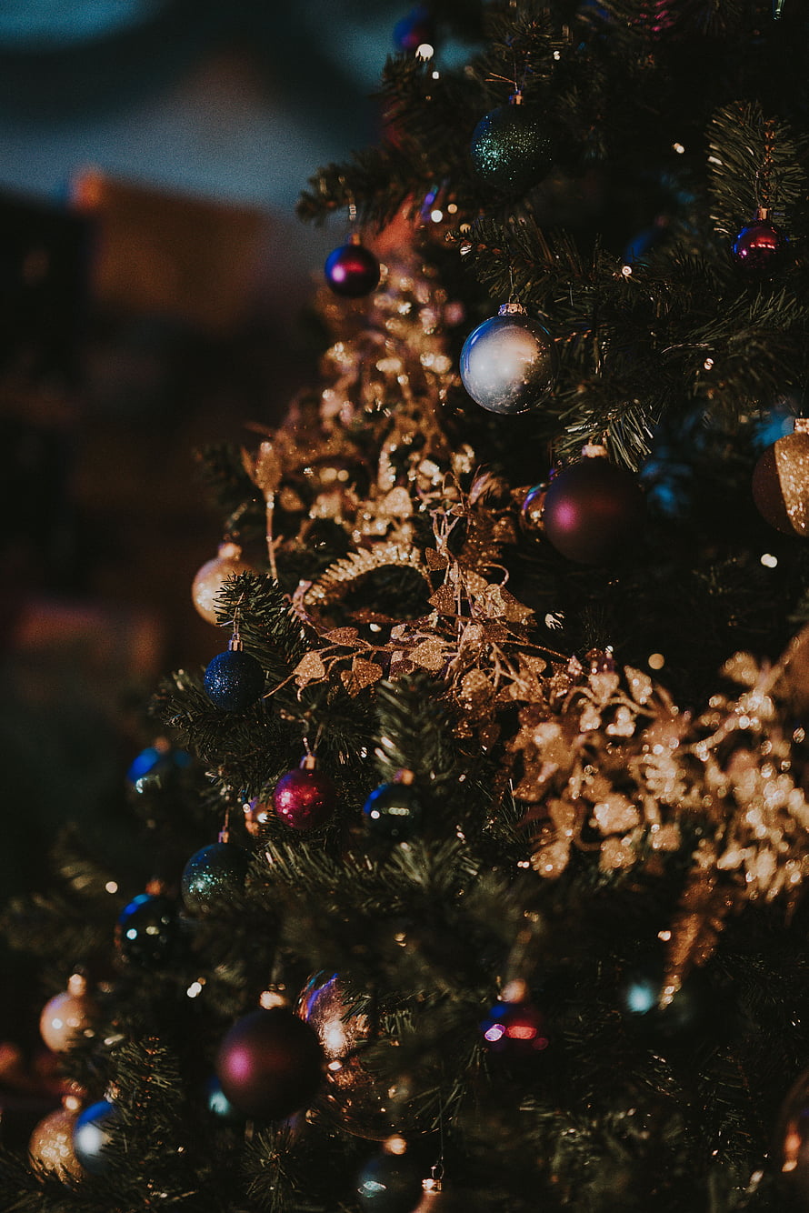 Close-up of a decorated Christmas tree with colorful baubles and golden tinsel in warm ambient light HD phone wallpaper