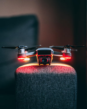 Compact Camera Drone With Glowing Red Navigation Lights Perched On Fabric Surface HD phone wallpaper