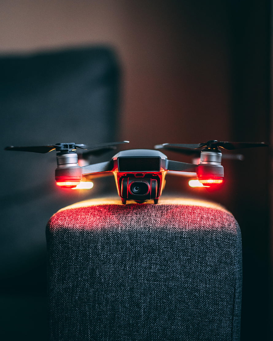 Compact Camera Drone With Glowing Red Navigation Lights Perched On Fabric Surface HD phone wallpaper