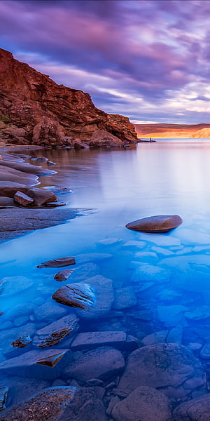 Serene Coastal Landscape with Smooth Rocks and Calm Blue Water at Dusk HD phone wallpaper