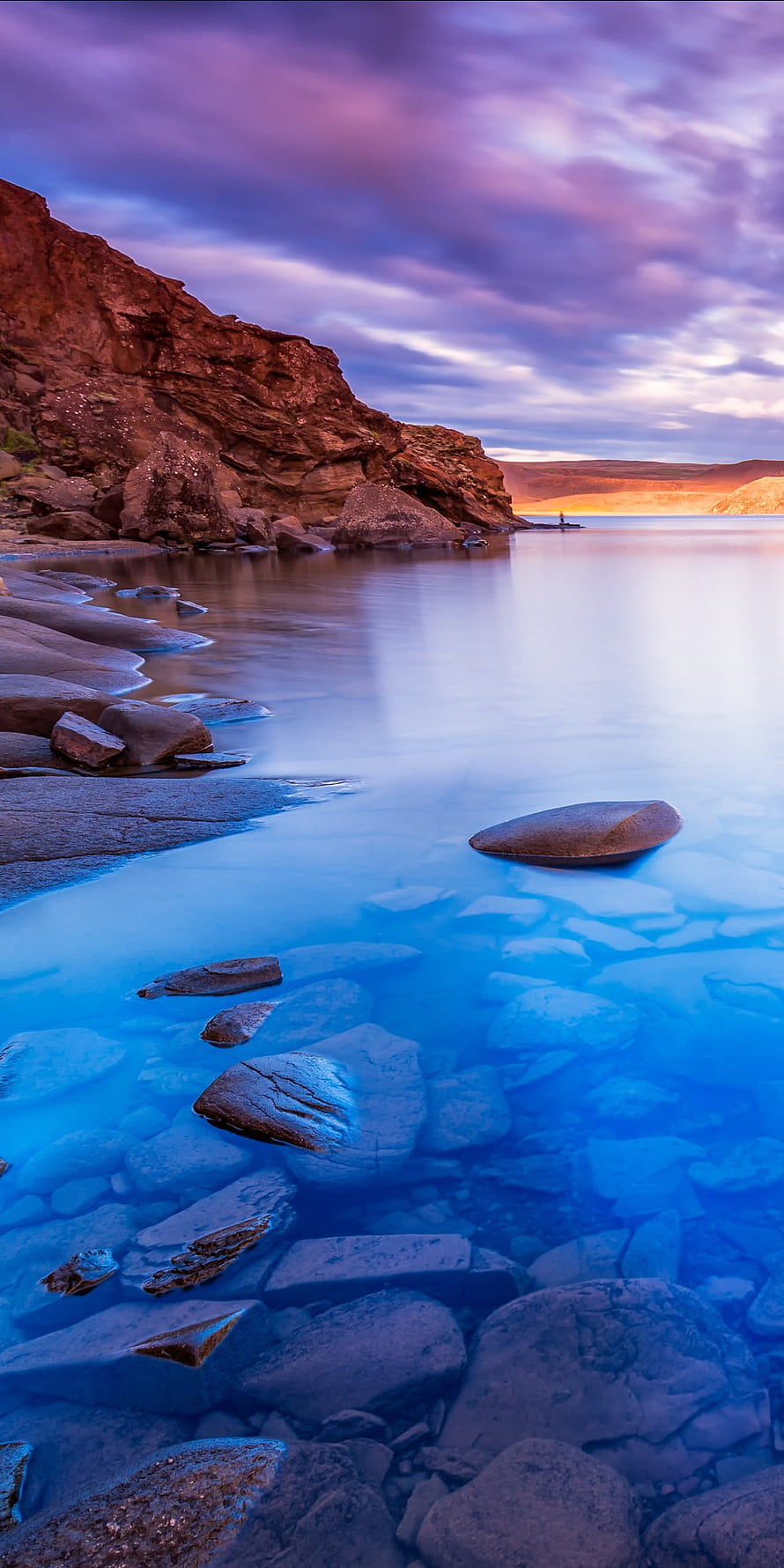 Serene Coastal Landscape with Smooth Rocks and Calm Blue Water at Dusk HD phone wallpaper