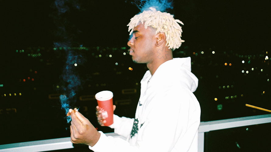 Ken Carson Smoking on a Rooftop at Night with City Lights in the Background HD wallpaper