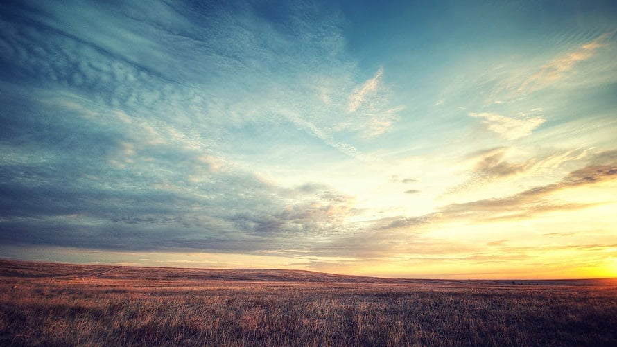 Vast Prairie Landscape at Golden Hour with Dramatic Clouds and Warm Sunset Glow HD wallpaper
