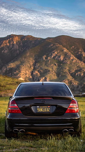 Rear View of a Black Mercedes-Benz W211 AMG Sedan Parked in a Mountain Meadow at Sunset HD phone wallpaper