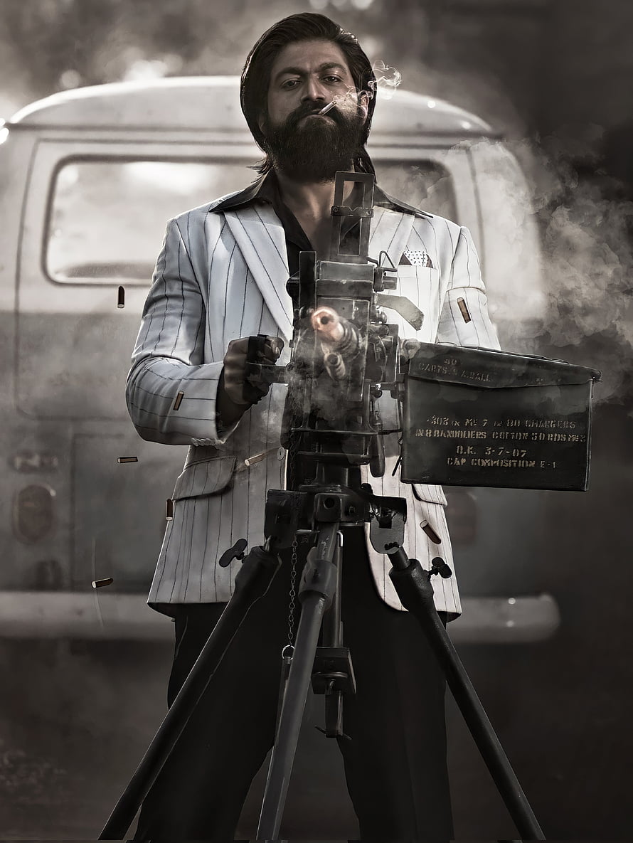 Rocky Bhai from KGF Chapter 2 in a white pinstripe suit firing a mounted machine gun HD phone wallpaper