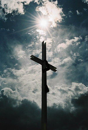 Silhouette of a wooden cross against a dramatic cloudy sky with the sun breaking through HD phone wallpaper