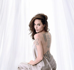 Angelina Jolie in a satin gown with back tattoos against a white curtain backdrop HD wallpaper