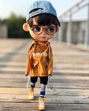 Stylized BJD Boy Doll in Orange Jacket and Blue Cap on Wooden Deck HD phone wallpaper
