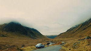 Skyfall Movie Scene: Vintage Car and Lone Figure on a Misty Highland Road HD wallpaper