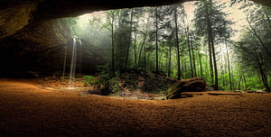 Misty forest waterfall viewed from a dark cave opening with lush green trees HD wallpaper