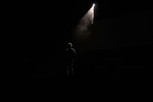 Lone Human Silhouette Standing in Darkness Beneath a Single Dramatic Spotlight Beam HD wallpaper