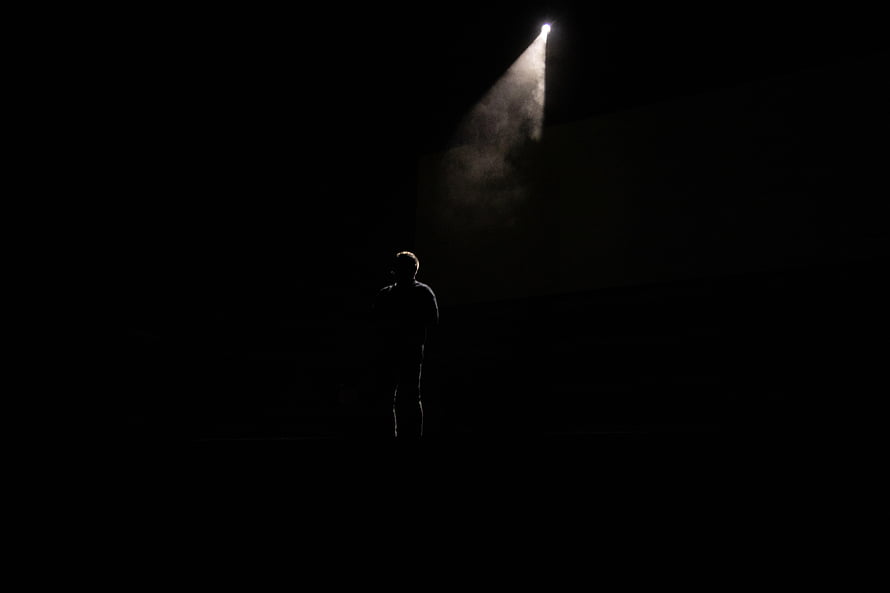 Lone Human Silhouette Standing in Darkness Beneath a Single Dramatic Spotlight Beam HD wallpaper