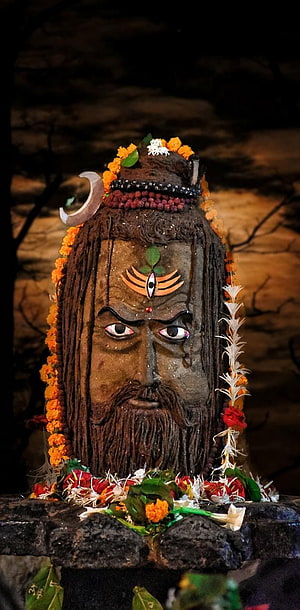 Mahakal deity statue adorned with marigold garlands and sacred offerings in a dark temple setting HD phone wallpaper