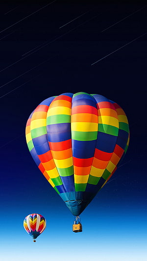 Vibrant rainbow striped hot air balloon floating in a deep blue sky with a second balloon in the distance HD phone wallpaper