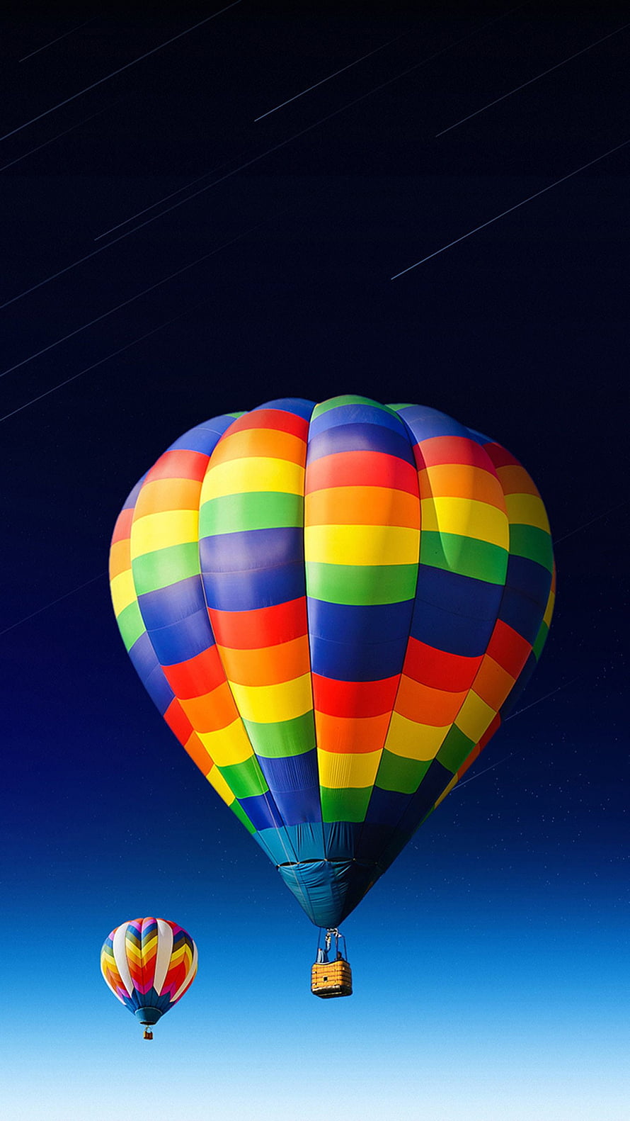 Vibrant rainbow striped hot air balloon floating in a deep blue sky with a second balloon in the distance HD phone wallpaper