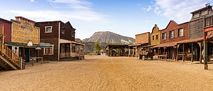Dusty Main Street of a Historic Old West Town with Wooden Buildings and Mountains HD wallpaper