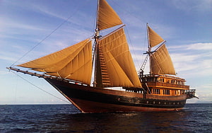 Traditional wooden sailing ship with golden sails on the open ocean under a blue sky HD wallpaper