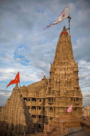 Dwarkadhish Temple in Dwarka India with ornate stone spires and fluttering flags under a cloudy sky HD phone wallpaper