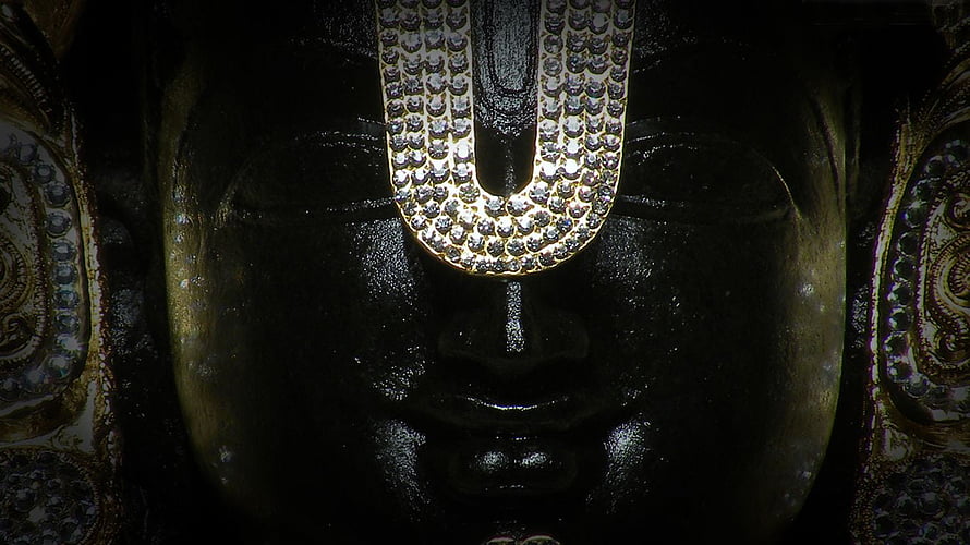 Close-up of Lord Venkateswara statue with ornate forehead ornament and dark polished surface HD wallpaper