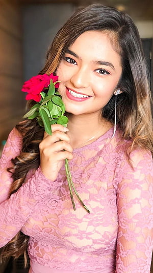 Anushka Sen smiling portrait holding red roses in a pink lace top HD phone wallpaper