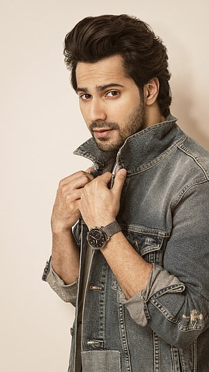 Varun Dhawan in a distressed denim jacket with a wristwatch against a neutral studio backdrop HD phone wallpaper